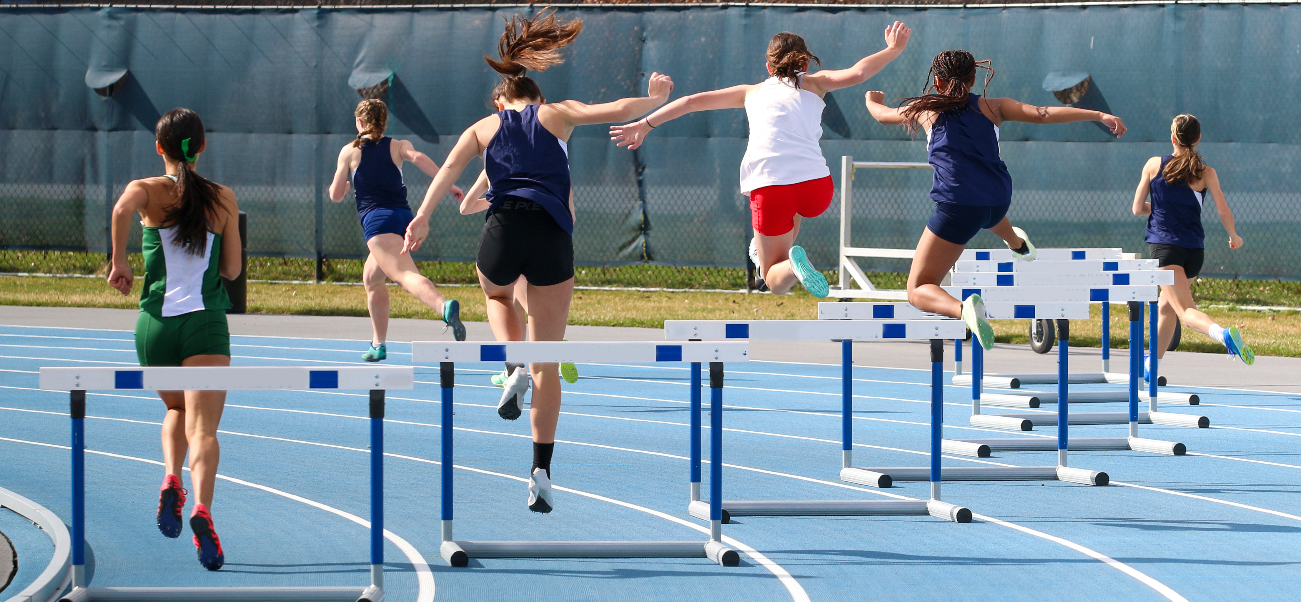 girls jumping hurdles at a high school track meet